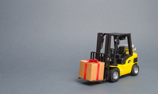 Yellow forklift truck carries a gift with a red bow. Purchase and delivery of a present. retail