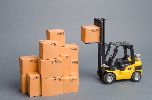 Yellow Forklift truck raises a cardboard box to the top of a stack pile of boxes. Warehouse, stock