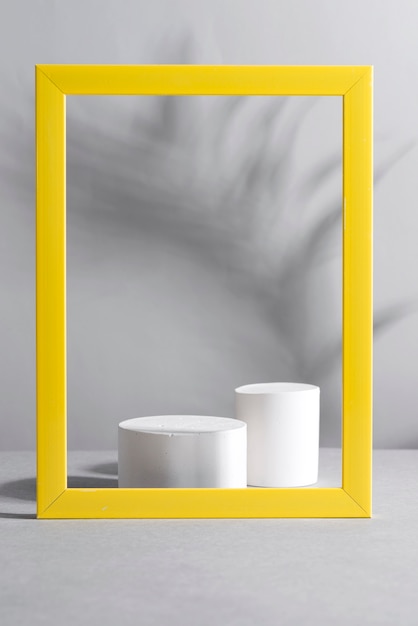 Yellow frame with palm shadows and white geometric podiums on grey table. Trendy colors 2021.