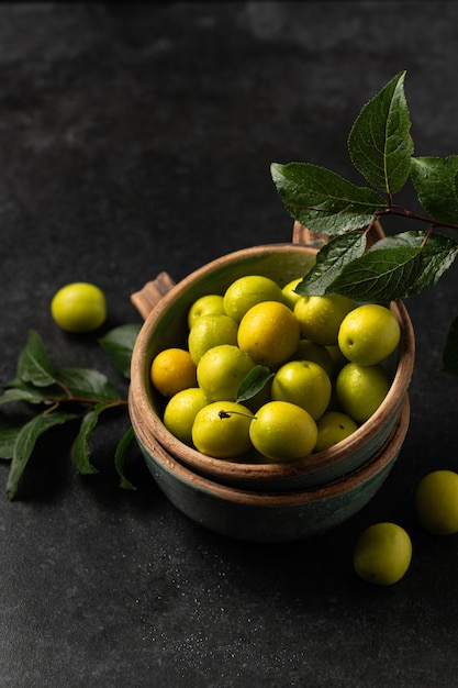 Yellow freshly torn cherry plum with green leaves in ceramic cups on a gray background, space for text