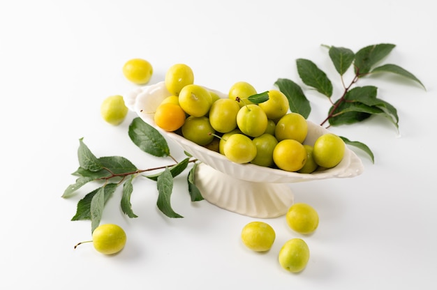 Yellow freshly torn cherry plum with green leaves in a ceramic vase on a white background