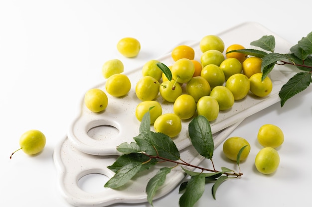 Yellow freshly torn cherry plum with leaves, ceramic boards for serving on a white background