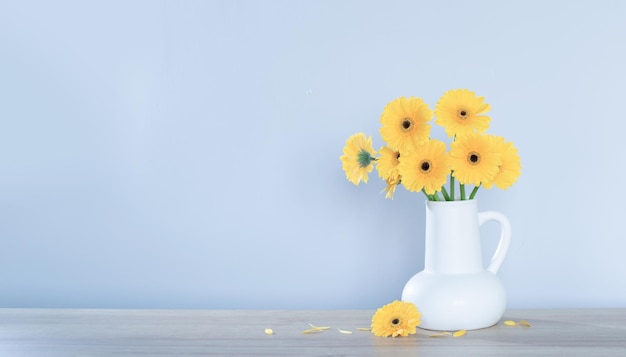 yellow gerbera in white jug on wooden shelf on background wall