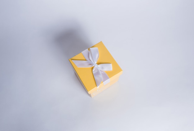 Yellow gift box with white ribbon on a white table