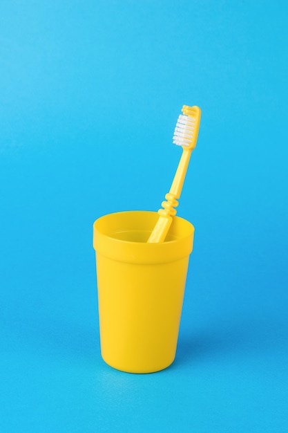 A yellow glass with a yellow toothbrush on a light blue background