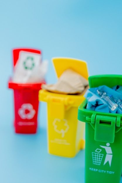 Yellow, green and red recycle bins with recycle symbol on blue background. Keep city tidy, Leaves the recycling symbol. Nature protection concept.