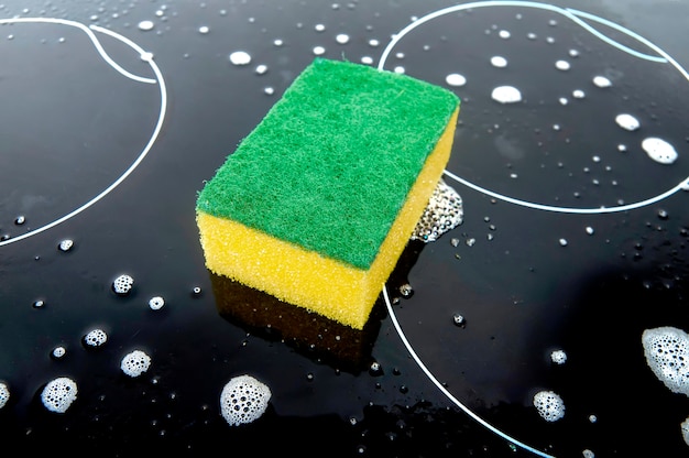 Yellow green sponge on the black surface of the hob and detergent foam