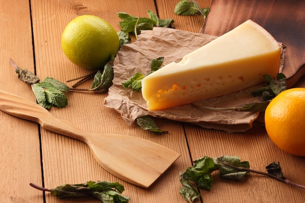 Yellow hard cheese on parchment paper A piece of cheese with citrus fruits dried mint on a wooden background Closeup