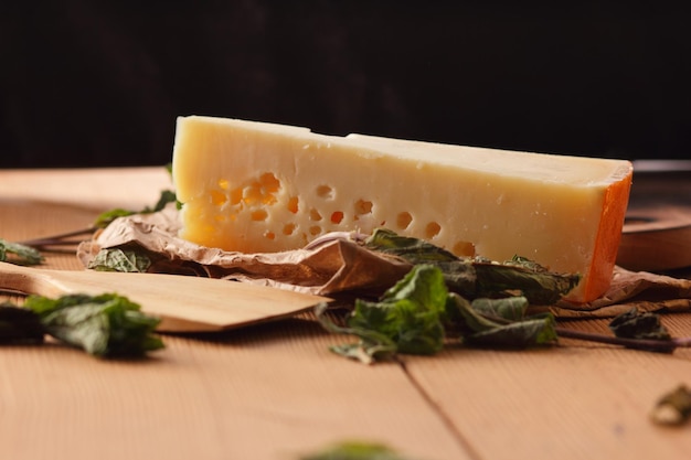 Yellow hard cheese on parchment paper A piece of cheese with citrus fruits dried mint on a wooden background Closeup