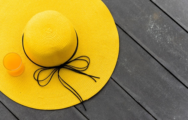 Photo yellow hat with fresh orange juice on the beach. summer vacation with space on wood background.