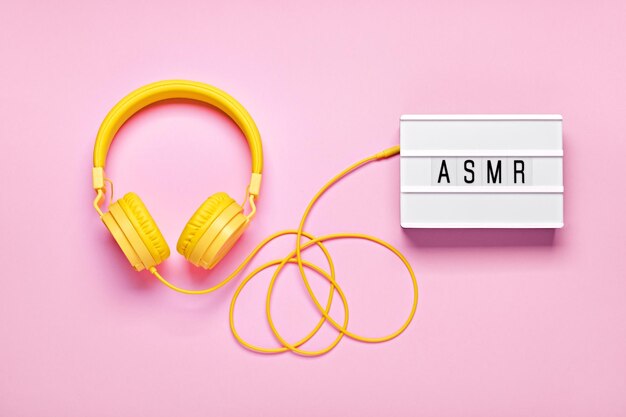 Yellow headphones and ASMR letters lightbox on pink background ASMR Stressrelieving sounds concept flat lay