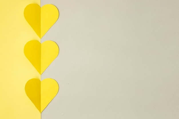 Yellow hearts cut out of colored paper on a gray background, top view, colors 2021. Trendy colored valentines day concept.