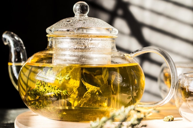 Yellow herbal tea in a transparent glass teapot and two bowls on a round wooden tray.