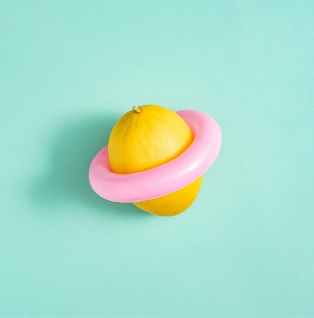 Yellow honeydew melon with pink swimming ring isolated on green background. Abstract. Minimalist concept. Square with copy space.