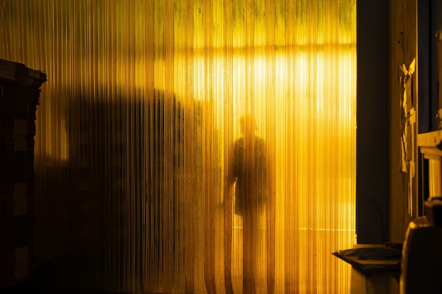 Yellow industrial plastic curtain entrance with shadow of worker and cardboard box package in warehouse