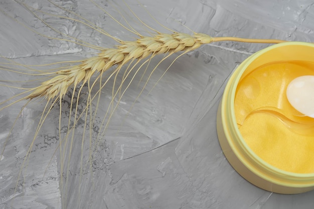 Yellow jar of eye patches and ear of wheat on gray background self care concept natural beauty woman