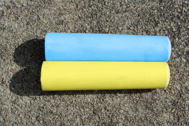 Yellow and light blue chalk sticks on asphalt flat lay