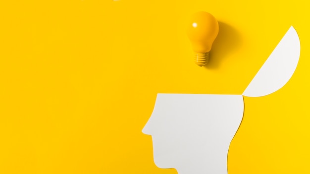 Yellow light bulb over the open paper cut out head against colored background