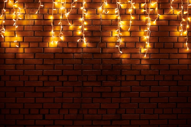 Yellow lights garlands hanging from red brick wall at evening beautiful christmas house decoration