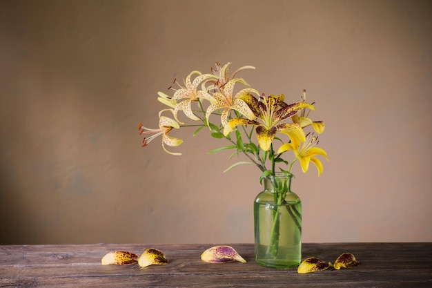 yellow lily in green glass vase on wooden table