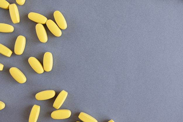 Yellow long vitamins or pills on gray background, closeup, copy space