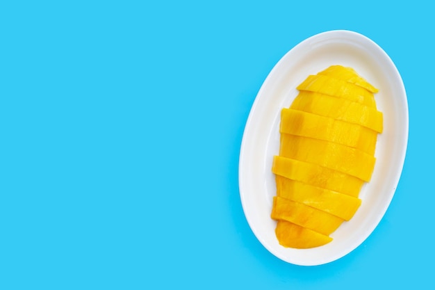 Yellow mango slices in white plate on blue background