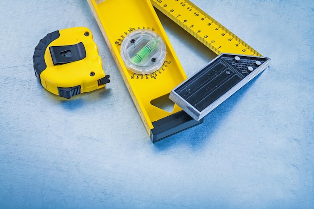 Yellow measuring tape construction level and square ruler on metallic background maintenance concept