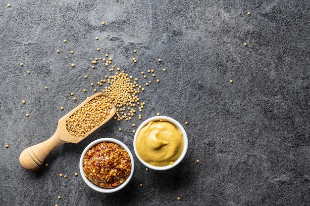 Photo yellow mustard and whole grain mustard and mustard seeds on kitchen table top view