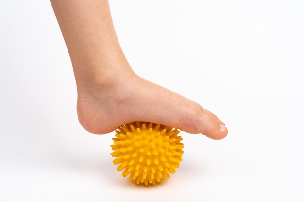 Yellow needle ball for massage and physical therapy on a white background with a child39s foot the concept of prevention and treatment of foot valgus