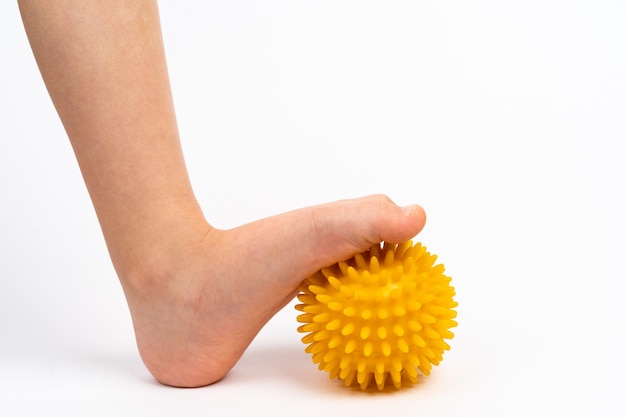 Yellow needle ball for massage and physical therapy on a white background with a childs foot the