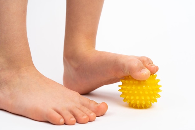 Yellow needle ball for massage and physical therapy on a white background with a childs foot the