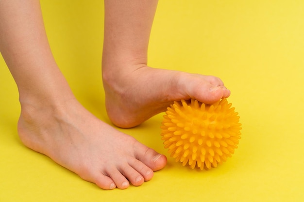 Yellow needle ball for massage and physical therapy on a yellow background with a childs foot the