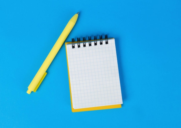 Yellow notepad with looseleaf paper and a pen on a blue background Empty page in a cell for text View from above