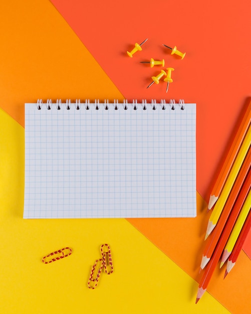 Yellow and orange office desk table with blank notebook and other office supplies. Top view with copy space, flat lay.