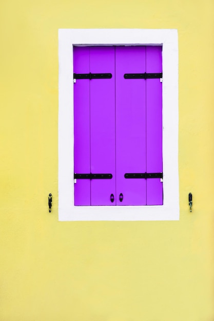 Yellow painted facade of the house and window with lavender shutters