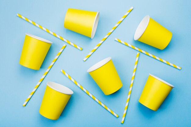 Yellow paper cups and yellow-white straw on blue. Top view