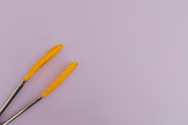 Yellow pasta tongs on purple background