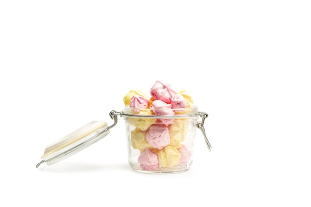 Yellow and pink meringues in a glass jar on a white background with copy space