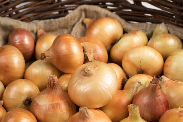 Yellow and pink onions in a basket on a bag.