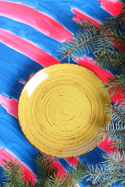 Yellow plate with spruce branches on a pinkblue background Closeup View from above Blank space for signature