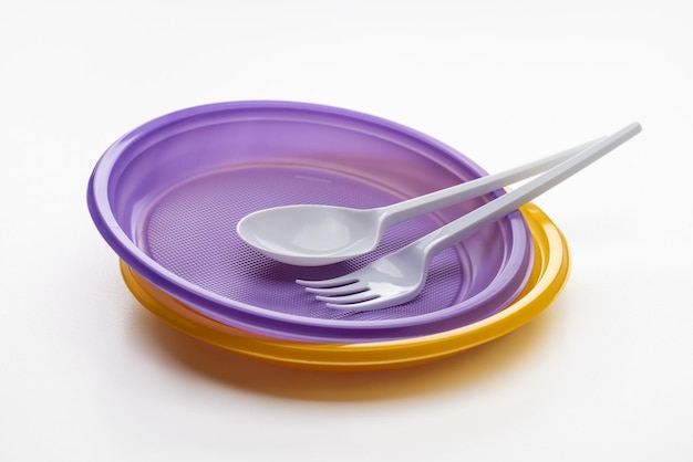 Yellow and purple plastic plates, fork and spoon on a white background.