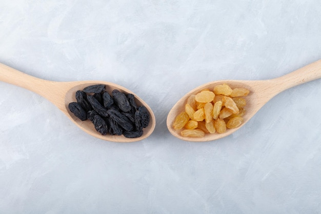 Yellow raisins and black raisins in wooden spoons on grey background top view Dried grapes fruit