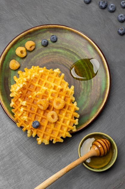 Yellow raspberries crispy waffles and drop of honey on plate Honey dipper in green bowl