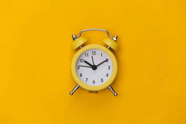 Yellow retro alarm clock on a yellow background. . Minimalism