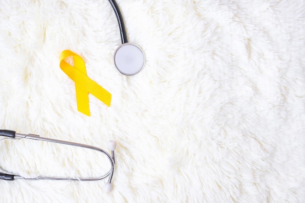 Yellow Ribbon and Stethoscope on white background for supporting people living and illness. September Suicide prevention day, Childhood Cancer Awareness month and World cancer day concept