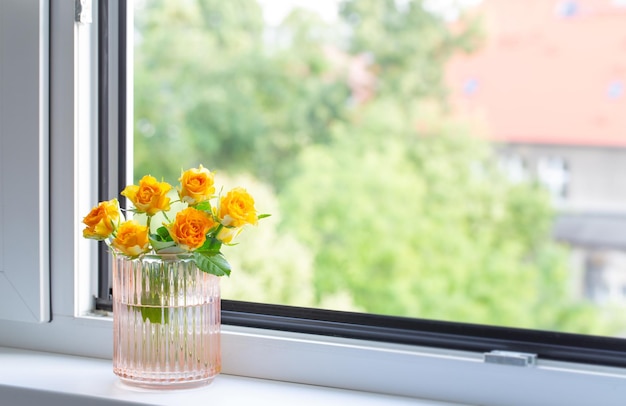 yellow roses in glass vase on windowsill