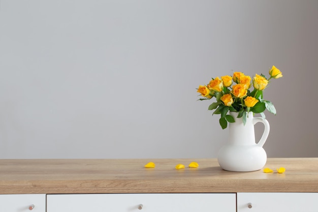 Yellow roses in white jug on wooden shelf