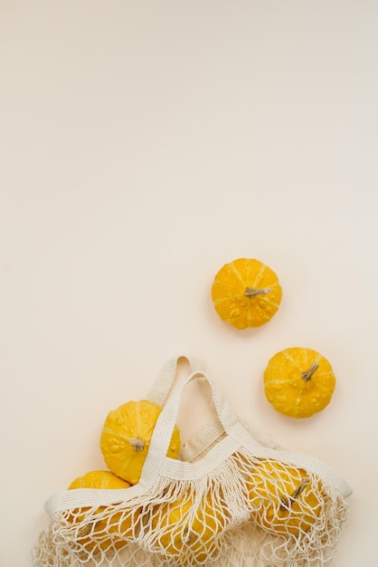 Yellow round small pumpkins in a mesh eco friendly bag on a light background Autumn composition