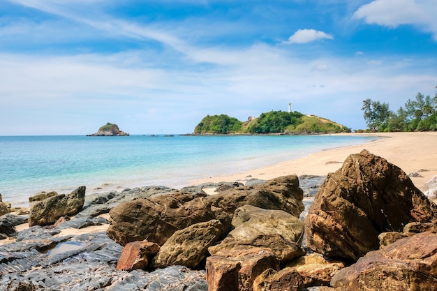 Yellow sand and large stones, turquoise sea and sky and a white lighthouse on a cliff