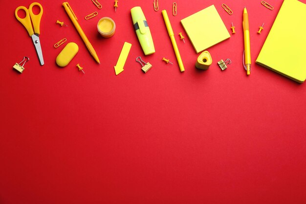 Yellow school stationery on red background flat lay Space for text